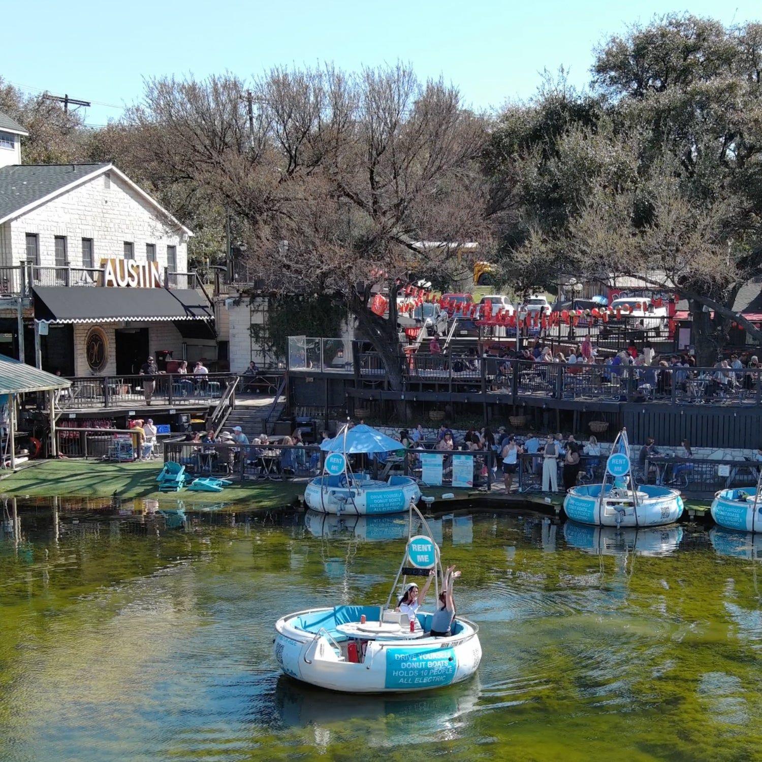 Mozart's seen from Lake Austin, the decks full and donut boats on the water
